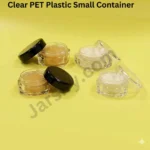 A clear, premium acrylic cosmetic jar with a glossy black cap containing a peach cream, balanced on a human index finger against a soft yellow background. Part of the 'all-in-one' 5g, 10g, and 20g empty jar collection.