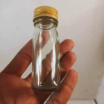 A tall and narrow transparent glass bottle is standing vertically on a country-style table.
