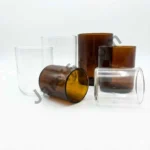 A high-quality comparison shot of two empty, straight-sided candle glass jars—one transparent clear and one deep amber. The image features professional dimension markings showing the mouth width and total length against a pure white background. candle jar