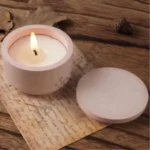 A close-up view of a person holding a small, solid yellow and multiple color and custom color matte-finish round concrete or stone candle jar, next to its separate flat circular lid. Text overlays show a height of 1.5 inches and width of 2.3 inches.