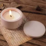 A close-up view of a person holding a small, solid yellow and multiple color and custom color matte-finish round concrete or stone candle jar, next to its separate flat circular lid. Text overlays show a height of 1.5 inches and width of 2.3 inches.