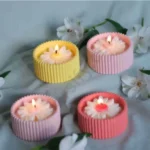 MarbleLuxe ribbed candle jars in blue, yellow, and white, made from solid marble powder, shown with lit candle flames on a split white and wood background. jarsify
