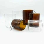 A high-quality comparison shot of two empty, straight-sided candle glass jars—one transparent clear and one deep amber. The image features professional dimension markings showing the mouth width and total length against a pure white background. candle jar